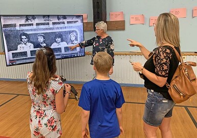 Melanie Winters and her children spot a familiar face on a school history video with the help of Administrative Assistant Malinda Bergen-Henengouwen during a farewell tour of Huntsville School.